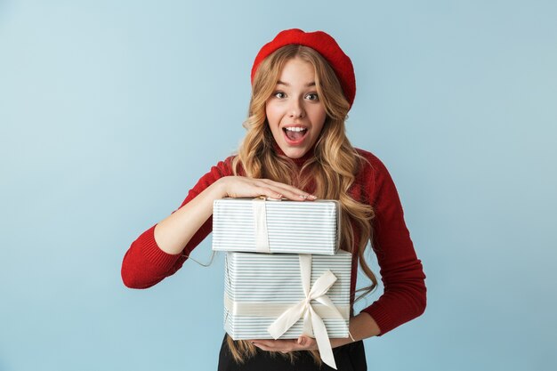 Imagen de mujer alegre 20s vistiendo boina roja sosteniendo cajas presentes aisladas