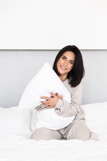 Imagen de mujer alegre de 30 años riendo, mientras se divierte con la almohada en la cama en casa