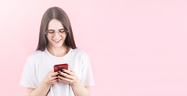 Imagen de mujer americana feliz sonriendo y usando teléfono celular aislado sobre pared rosa con copyspace