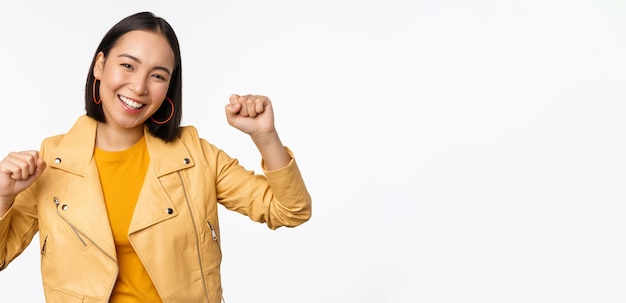 Imagen de mujer asiática bailando y sonriendo feliz celebrando la victoria triunfando de pie sobre fondo blanco.