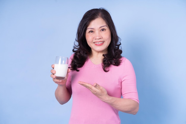 Imagen de una mujer asiática de mediana edad bebiendo leche con fondo azul