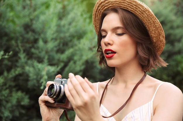 Imagen de mujer de belleza en vestido y sombrero de paja con cámara retro al aire libre