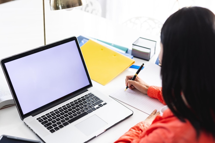 Foto imagen de una mujer biracial usando una computadora portátil con espacio de copia en la pantalla sentada en el escritorio