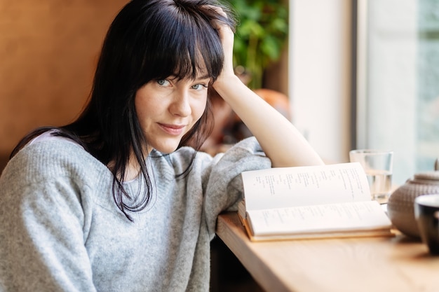 Imagen de una mujer bonita joven sentada en la mesa de café y libro de lectura. niña en el café, libro, lectura, café