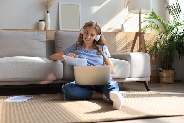 Imagen de una mujer bonita que trabaja con la computadora portátil mientras está sentado en el piso en casa.