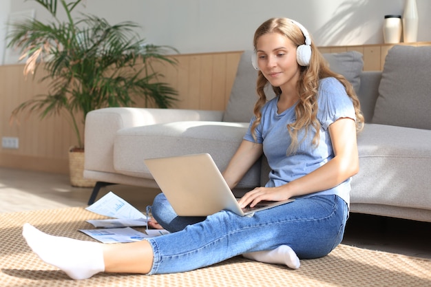 Imagen de una mujer bonita que trabaja con la computadora portátil mientras está sentado en el piso en casa.