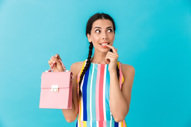 Imagen de mujer caucásica de pensamiento con coletas sosteniendo una bolsa rosa y mirando a un lado aislado sobre la pared azul