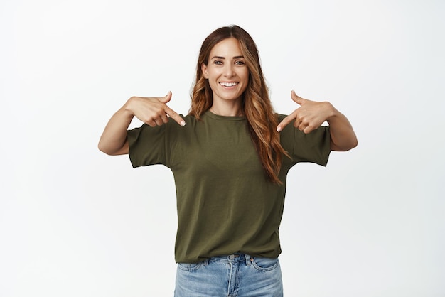 Foto imagen de una mujer caucásica sonriente señalando con el dedo en el centro que muestra la promoción de venta de la pancarta del logotipo recomendando publicidad de pie sobre fondo blanco