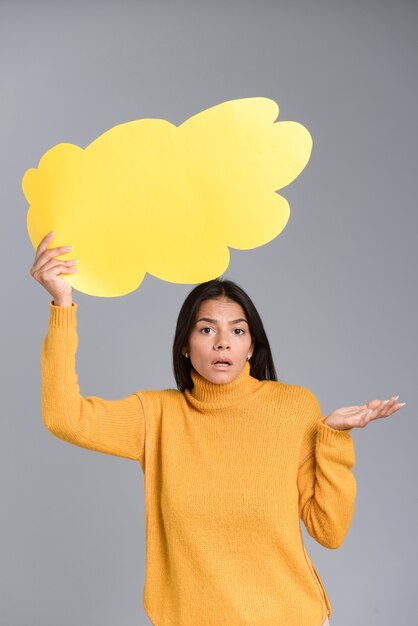 Imagen de una mujer confundida posando aislada sobre pared gris con globo.