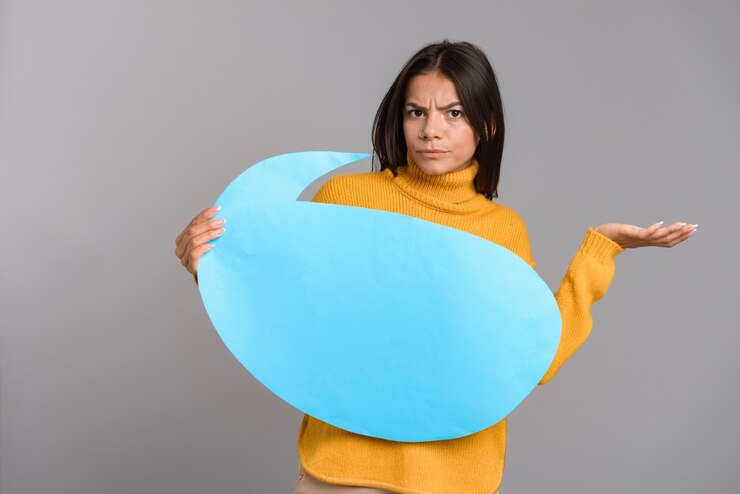 Foto imagen de una mujer confundida posando aislada sobre pared gris sosteniendo bocadillo.