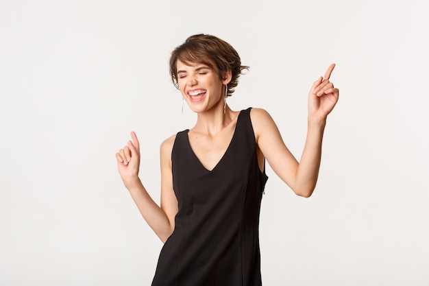 Imagen de mujer elegante despreocupada divirtiéndose, bailando y cantando, de pie sobre blanco.