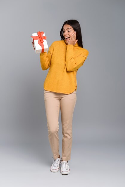 Imagen de una mujer emocionada feliz posando aislada sobre pared gris con caja sorpresa presente.