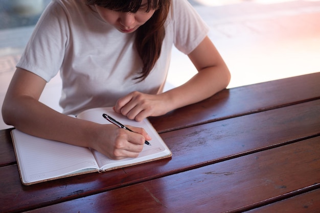 Imagen de una mujer escribiendo en un cuaderno en blanco sobre la mesa.