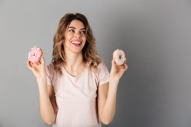 Imagen de mujer feliz en camiseta mostrando donas y mirando a otro lado sobre gris