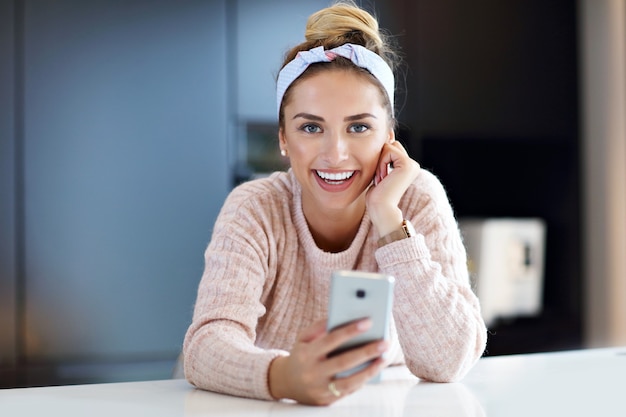 Imagen de mujer feliz enviando mensajes de texto en la cocina