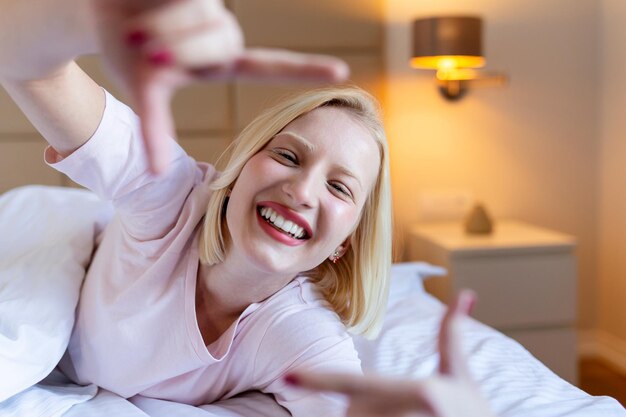 Imagen de una mujer haciendo el signo de un marco de fotos con los dedos mientras está acostada en la cama