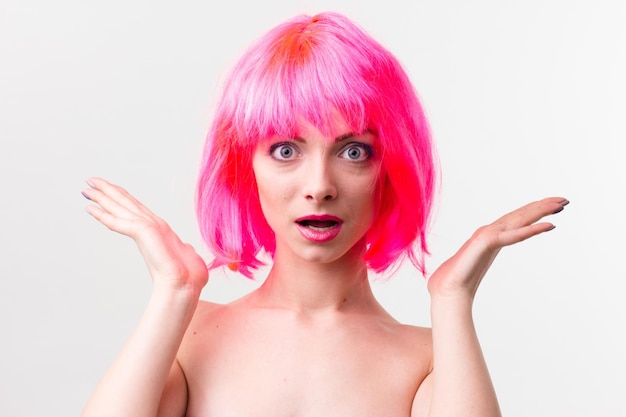 Imagen de una mujer hermosa y emocionada con peluca riéndose mientras posa con dulces aislados sobre un fondo rosa