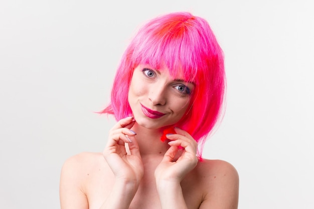 Imagen de una mujer hermosa y emocionada con peluca riéndose mientras posa con dulces aislados sobre un fondo rosa