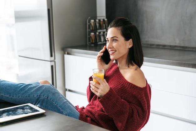 Imagen de una mujer increíble en el interior de su casa en la cocina hablando por teléfono móvil.