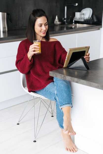 Imagen de una mujer increíble en el interior de su casa en la cocina con tablet PC bebiendo jugo.