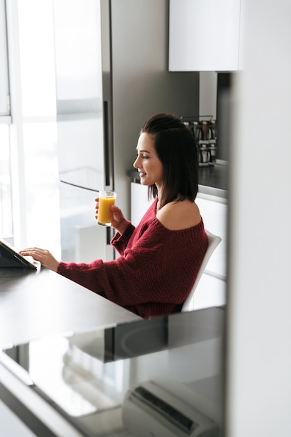 Imagen de una mujer increíble en el interior de su casa en la cocina con tablet PC bebiendo jugo.
