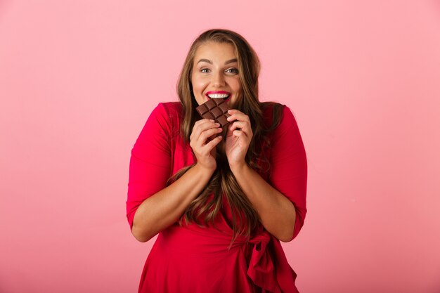 Imagen de una mujer joven bastante hambrienta aislada sobre pared rosa con chocolate.