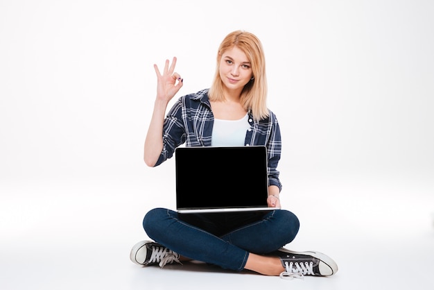 Imagen de una mujer joven y bonita que usa la computadora portátil aislada en un fondo blanco mientras hace el gesto bien.