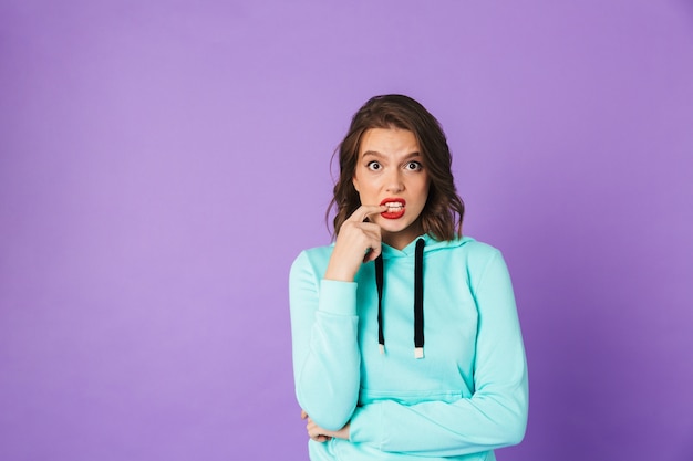 Imagen de una mujer joven emocional confundida posando aislada sobre la pared púrpura.