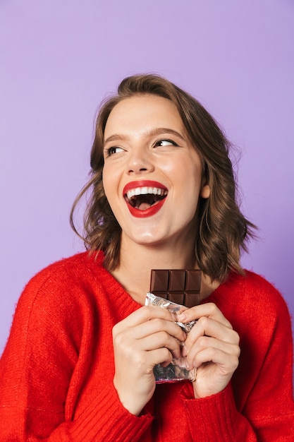 Imagen de una mujer joven emocional conmocionada posando aislada sobre la pared de la pared púrpura con chocolate.