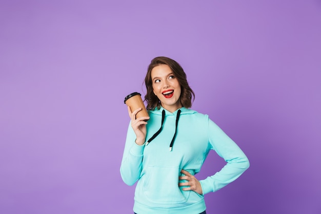 Imagen de una mujer joven hermosa emocionada posando aislada sobre la pared de la pared púrpura tomando café.