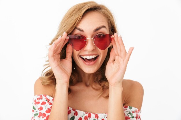 Imagen de mujer joven positiva sorprendida en gafas de sol posando aislada sobre pared blanca.