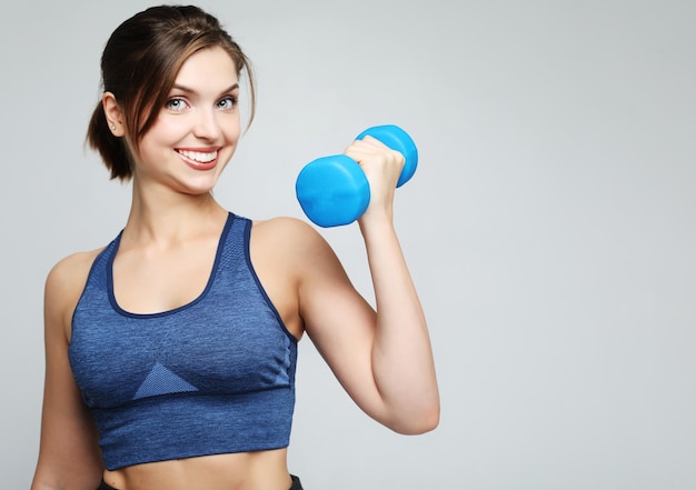 Imagen de una mujer joven sana y en forma sonriendo y sosteniendo dumbbelsl al hombro Concepto de deporte y personas