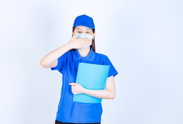 Imagen de mujer joven en uniforme con carpeta y máscara médica.