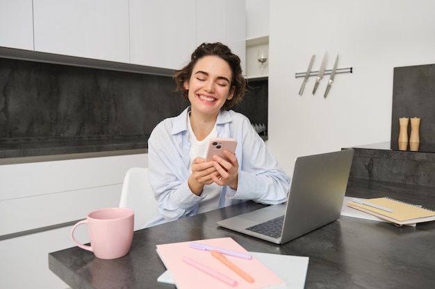 Imagen de una mujer joven usando su teléfono inteligente en casa una niña se sienta con un teléfono móvil en la cocina y sonríe