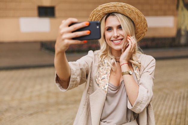 Imagen de una mujer linda joven feliz caminando al aire libre tomar un selfie por teléfono móvil.