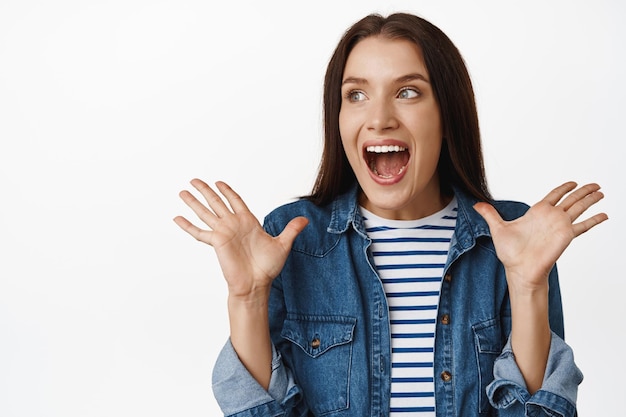 Foto la imagen de una mujer morena sincera muestra una sorpresa genuina, mirando a un lado con las manos levantadas por noticias agradables e inesperadas, regocijándose, su gran anuncio, fondo blanco