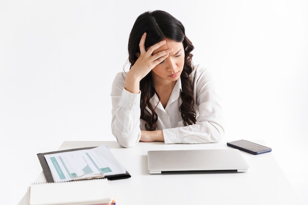 Imagen de mujer de negocios asiática molesta o cansada vistiendo ropa de oficina sentado en la mesa con un portátil y agarrando la cabeza