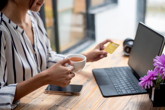 Imagen de una mujer de negocios sentada y tomando café sosteniendo una tarjeta de crédito comprando en línea usando una tableta y teléfonos inteligentes colocados en la mesa