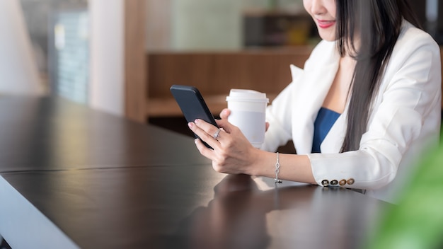 Imagen de una mujer de negocios sonriente feliz tomando café mirando un teléfono inteligente en un café.