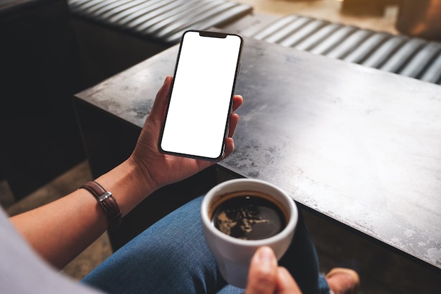 Imagen de una mujer que sostiene un teléfono móvil con una pantalla de escritorio blanca en blanco mientras bebe café