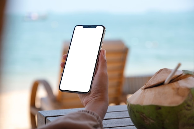 Imagen de una mujer que sostiene un teléfono móvil con una pantalla de escritorio en blanco mientras está sentada en la playa