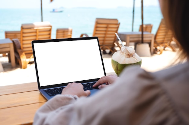 Imagen de una mujer que usa y escribe en una computadora portátil con una pantalla de escritorio en blanco mientras está sentada en la playa