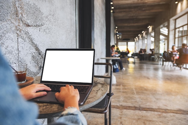 Imagen de una mujer que usa y escribe en el teclado de una computadora portátil con una pantalla de escritorio en blanco en un café