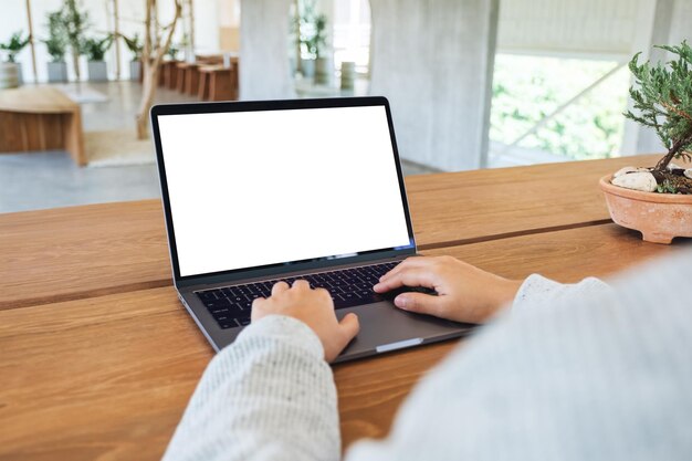 Imagen de una mujer que usa y escribe en el teclado de una computadora portátil con una pantalla de escritorio en blanco en una mesa de madera