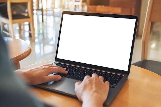 Imagen de una mujer que usa y escribe en el teclado de una computadora portátil con una pantalla de escritorio en blanco en una mesa de madera