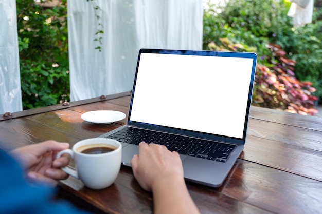 Imagen de una mujer que usa y toca el panel táctil de una computadora portátil con una pantalla de escritorio blanca en blanco mientras bebe café al aire libre