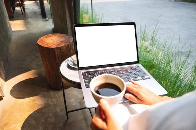 Imagen de una mujer que usa y toca el panel táctil de una computadora portátil con una pantalla de escritorio blanca en blanco mientras bebe café en un café