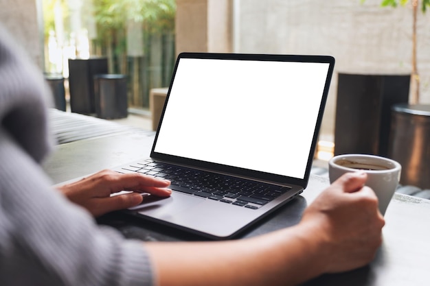 Imagen de una mujer que usa y toca el panel táctil de una computadora portátil con una pantalla de escritorio blanca en blanco mientras bebe café