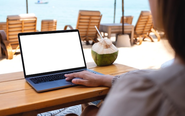 Imagen de una mujer que usa y toca el panel táctil de una computadora portátil con una pantalla de escritorio en blanco mientras está sentada en la playa