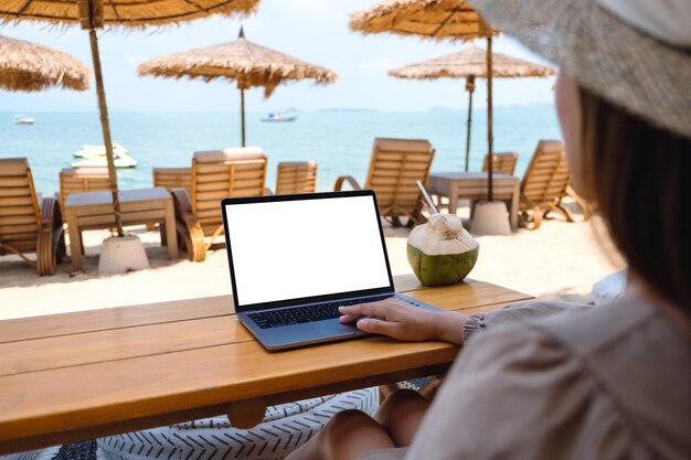 Imagen de una mujer que usa y toca el panel táctil de una computadora portátil con una pantalla de escritorio en blanco mientras está sentada en la playa